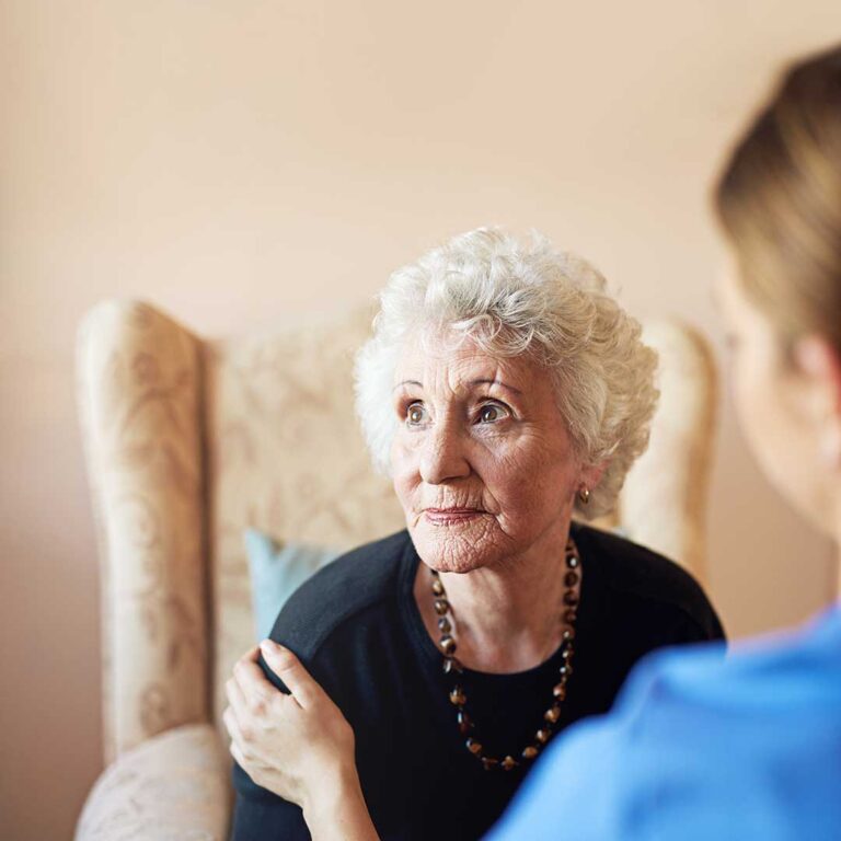 Care coordinator reviews a resident’s medication list with an older adult and family member at a table.